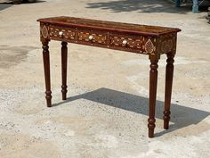 an old wooden table with carvings on the top and legs, sitting in dirt area