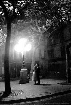 a man and woman standing in the middle of a street at night under a lamp post