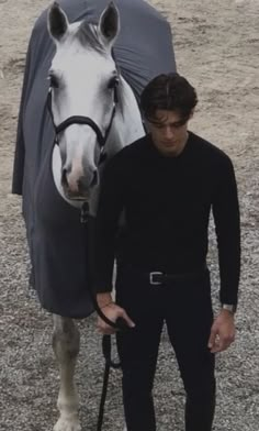 a man standing next to a horse with a blanket on it's head and holding the reins