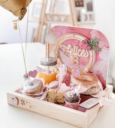 a wooden box filled with lots of food on top of a white table next to balloons