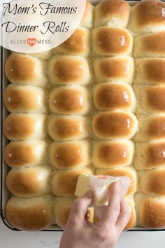 a person holding a piece of bread in front of a pan with rolls on it