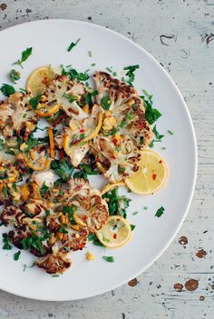 a white plate topped with meat and veggies next to a slice of lemon