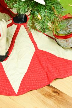 a red and white christmas tree skirt sitting on top of a wooden table next to a potted plant