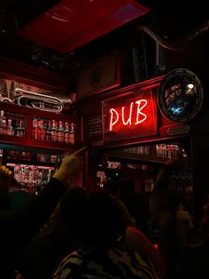 people are sitting at a bar with red neon signs on the wall and shelves full of liquor bottles