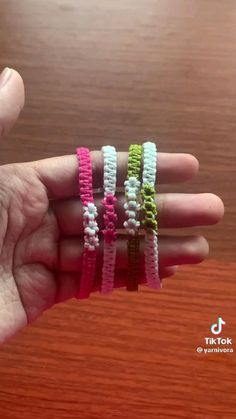 three different colored bracelets are held in someone's hand on a wooden table