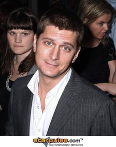 a man in a suit and white shirt standing next to other people at an event