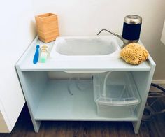 a white sink sitting on top of a wooden floor next to a trash can and bucket