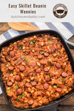 a skillet filled with beans and sausages on top of a wooden table next to a