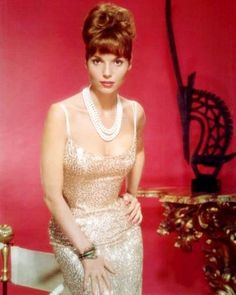 a woman in a dress and pearls posing for a photo with a red wall behind her