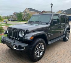 a black jeep parked in front of a house on a brick driveway next to a lamp post