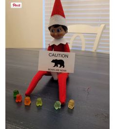 an elf is sitting on the table with gummy bears in front of him and holding a sign that says caution