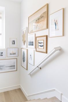 there are many framed pictures on the wall above the stairs in this room, and one is leaning up against the railing