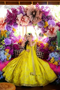 a woman in a yellow dress sitting on a bench with flowers around her and holding an umbrella