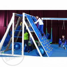 two children playing on a blue and white play set with swings, slides and balls