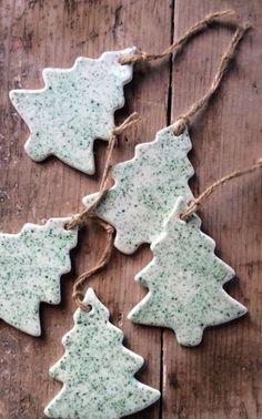 four ceramic christmas tree ornaments hanging from twine on wooden planks with jutting twine