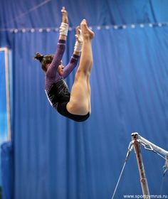 a woman is doing an acrobatic trick on the balance beam in front of a blue curtain