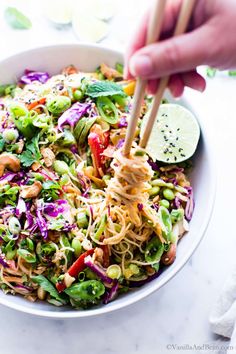 someone holding chopsticks over a colorful salad in a white bowl on a table