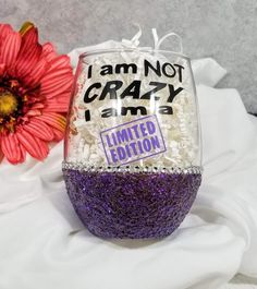 a purple and white glittered wine glass with i am not crazy on it next to a flower