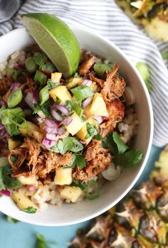 a white bowl filled with rice, meat and veggies next to sliced pineapples