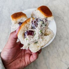 a hand holding a half eaten sandwich with meat and grapes on it, sitting on a white plate