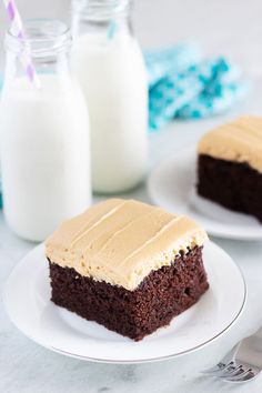 two pieces of chocolate cake with frosting on white plates next to milk bottles and utensils