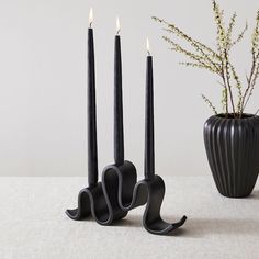 three black candles sitting on top of a table next to a vase filled with flowers