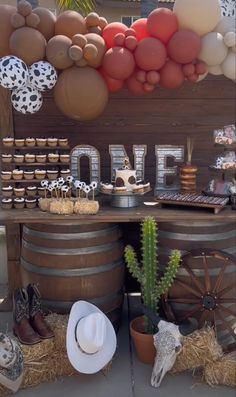 a table topped with lots of desserts and balloons in the shape of letters on top of wooden barrels