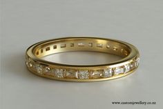 a yellow gold wedding band with princess cut diamonds on the inside and outside, set against a plain white background