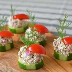 small cucumbers topped with tuna and tomatoes on a wooden cutting board, garnished with fresh dill