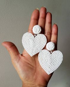 two white beaded hearts are held in the palm of a person's hand