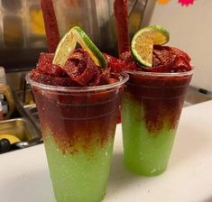 two cups filled with different colored drinks on top of a white counter topped with lime slices