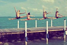 four people are jumping off the dock into the water