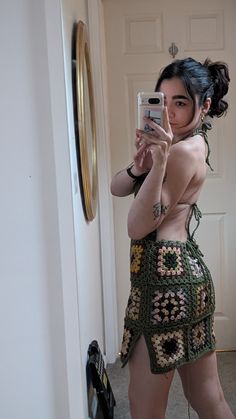 a woman taking a selfie in front of a mirror with her cell phone while wearing a crocheted skirt