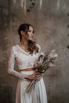 a woman in a white top and skirt holding dried flowers with her hands on her hips