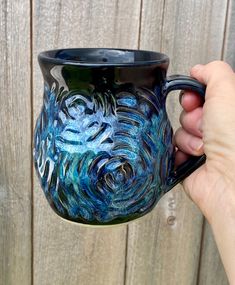 a hand holding a blue and black coffee mug with swirls on the inside, against a wooden fence