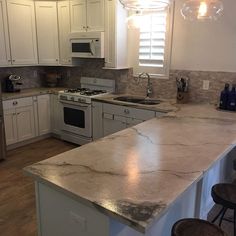 a kitchen with white cabinets and marble counter tops, along with an island in the middle