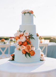 a wedding cake with orange and white flowers on the top is sitting on a table