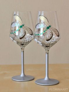 two wine glasses sitting on top of a table next to each other with designs on them