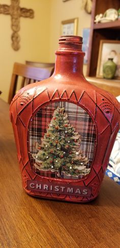 a bottle with a christmas tree on it sitting on a table in front of a cross