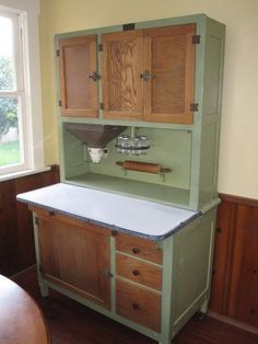 an old fashioned kitchen with wooden cabinets and white counter top, in front of a window