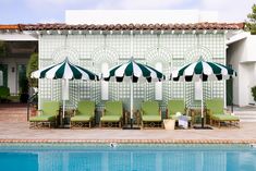 an outdoor pool with chairs and umbrellas next to the side of a white building