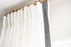 a white curtain with black greek border hanging from a rod