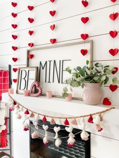 valentine's day mantel decorated with red and white heart garlands, candles, potted plant and sign that says be mine