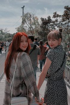 two young women holding hands and walking down a sidewalk with people in the background on a cloudy day