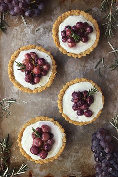 four small pies with grapes and rosemary sprigs on a baking sheet, ready to be eaten