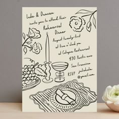 a white card with black ink on it next to a bowl of flowers and a candle