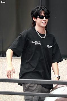 a young man wearing sunglasses and a black t - shirt is walking down the street