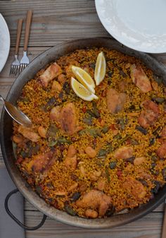 a pan filled with rice and chicken on top of a wooden table next to silverware