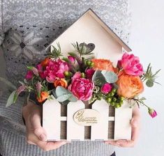 a person holding a house shaped box with flowers in it