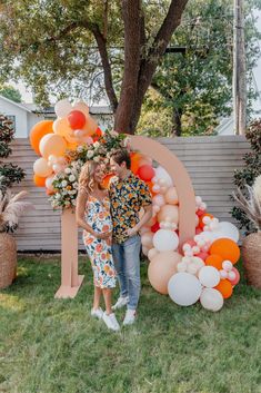 a man and woman standing next to each other in front of a large balloon arch